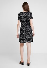 Svart kortärmad klänning med vitt abstrakt prickmönster, figursydd midja och utställd kjol. Bärs med svarta klacksandaler med blockklack.