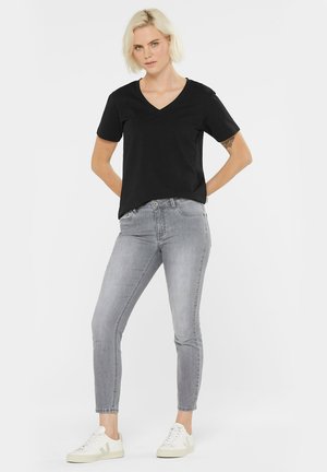 Schwarzes V-Ausschnitt-T-Shirt kombiniert mit hellgrauen Slim-Fit-Jeans und weißen Sneakers. Baumwollmaterial, kurze Ärmel und lässige Passform.
