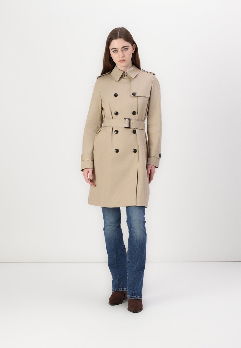 Beige trenchcoat met dubbelzijdige knopen, riem en schouderstukken. Gecombineerd met blauwe flared jeans en bruine chelsea boots. Eenvoudig, gestructureerd ontwerp.