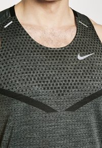 Débardeur Nike noir et gris présentant une texture à motifs, des accents de design en forme de V et un logo réfléchissant sur la poitrine.