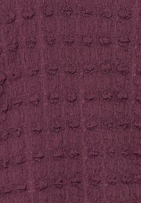 Tkanka w ciemnym burgundzie z teksturowanym wzorem z uniesionymi, okrągłymi motywami. Powierzchnia wydaje się miękka i pleciona, z delikatnym blaskiem.