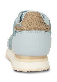 Zapatilla deportiva azul claro con una parte trasera tejida texturizada, tela suave, forma redondeada y una mediasuela blanco crema con rayas sutiles.