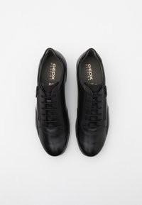 Scarpe in pelle nera con finitura liscia, caratterizzate da un design con lacci e una cerniera laterale, sovrapposte a un pannello in rete per la traspirabilità.