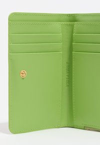 Interior de monedero de cuero verde con seis ranuras para tarjetas, un cierre metálico a presión y el nombre de la marca en relieve "BIMBA Y LOLA". Textura suave.