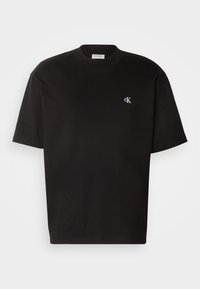 Czarna bawełniana koszulka z okrągłym dekoltem, krótkimi rękawami i białym haftowanym logo na lewej piersi. Gładka tekstura, standardowy krój.