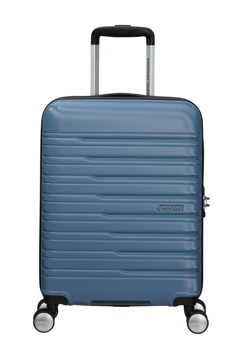 Valise bleue rigide avec une texture en relief, poignée rétractable et quatre roulettes. Équipée d'une fermeture éclair et d'un logo sur le devant.