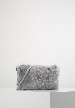 Grå rektangulær håndtaske i kunstpels med en tynd rem, der hviler på en hvid overflade mod en ensartet grå baggrund.