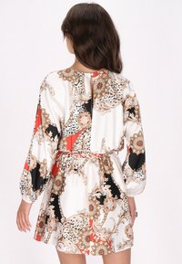 Bloemenpatroon jurk in het wit, rood en zwart met lange mouwen, verzamelde taille en een sleufdetail op de rug. Glad stoftextuur.