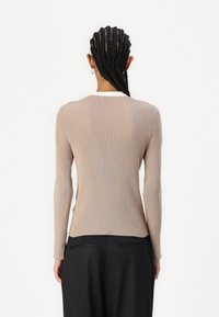 Long-sleeve beige ribbed top with a white collar, featuring a fitted design and textured fabric. Worn with black high-waisted pants.