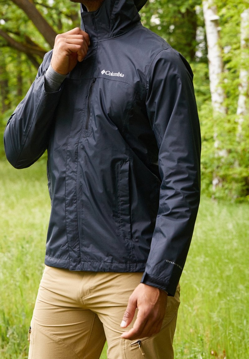 Wasserabweisende marineblaue Jacke mit hohem Kragen, Reißverschluss und dezentem Branding. Leichter Stoff mit glatter Textur.