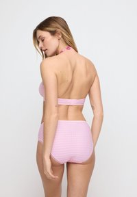 Pink halter bikini top paired with matching high-waisted bottoms, featuring textured pattern and adjustable clasp at the back.