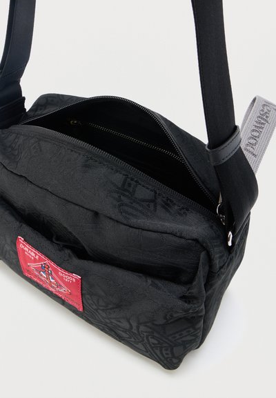 Μαύρο τσαντάκι crossbody με γεωμετρικά σχέδια, κόκκινο λογότυπο σε πατς, κύριο διαμέρισμα με ανοιχτό φερμουάρ, μπροστινή τσέπη και ρυθμιζόμενο λουρί ώμου.