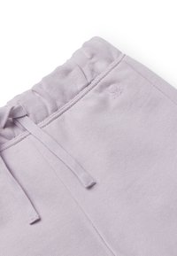 Světle fialový elastický pás tepláků se šňůrkou a jemně vyšitým malým logem na pozadí z měkké látky.