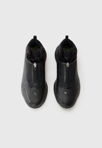 Melnas sporta kurpes ar rāvējslēdzi priekšā, teksturētu auduma augšdaļu, mīkstinātu apmalīti un gumijas zoli. Iekļauj diskretus logotipu akcentus.