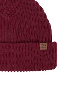 Czerwona dzianinowa czapka typu beanie z prążkowaną fakturą, zwiniętym mankietem i małą, brązową skórzaną metką z logo.