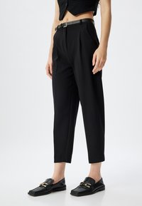 Pantaloni neri su misura con pieghe, lunghezza cropped e una cintura elegante. Abbinati a mocassini neri con finitura testurizzata e dettagli in oro.