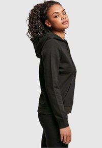 Black zip-up hoodie made of soft fabric with a kangaroo pocket, featuring ribbed cuffs and hem, and a fitted design.