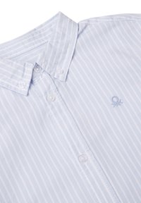 Camisa a rayas azul claro con cuello abotonado, con botones blancos y un pequeño logo bordado en el pecho. Textura suave.