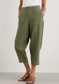 Vihreät pellavasekoitteiset cropped-housut, joissa on laskostettu etuosa, kaksi sivutaskua ja nappikiinnitys. Yhdistetty ruskeisiin remmikenkiin.