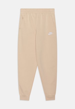 Pantalones de chándal Nike beige con cintura elástica, bolsillos laterales, puños acanalados y un logo blanco en el muslo izquierdo. Textura de tela suave.