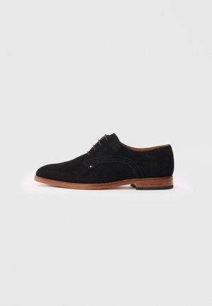 Pantofi oxford din nubuc negru cu o finisare netedă, bot rotund, cinci ochiuri și o talpă maro cu detaliul logo-ului mărcii.