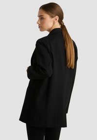 Schwarzes Blazer mit einem eleganten, taillierten Design. Verfügt über einen Reverskragen, lange Ärmel und zwei seitliche Taschen. Glatte Stofftextur.