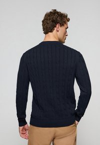 Marintrådad kabelstickad tröja med långa ärmar, ribbade ärmslut och ribbade midja, som visar upp ett strukturerat mönster över hela.