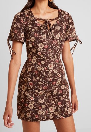 Floral dress in brown fabric featuring short puff sleeves, a square neckline with a tie detail, and an all-over floral pattern in cream and pink.