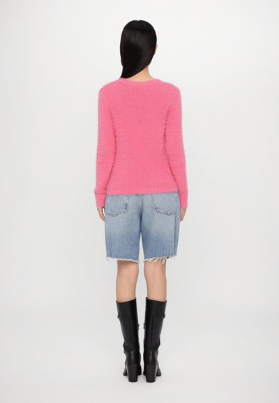 Suéter rosa difuso con mangas largas, combinado con pantalones cortos de mezclilla desgastados con bajos deshilachados y botas negras de tacón alto hasta la rodilla.