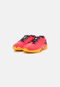 Chaussures de sport rouges et noires avec une tige texturée, des lacets noirs et des semelles en caoutchouc jaunes. Présente un logo sur le côté.