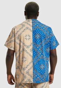 Camicia a maniche corte con un design a pannelli in tessuto a fantasia beige e blu, con intricati motivi paisley e sottili pois.