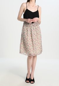 Camiseta de satén negra con tirantes finos, combinada con una falda floral de longitud a la rodilla en beige claro, con patrones en rosa y verde.