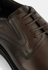 Chaussure habillée en cuir marron avec une texture lisse, dotée d'un laçage, de surpiqûres sur les côtés et d'un logo discret près de la languette.