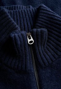 Granatowy sweter z prążkowanego dzianiny z wysokim kołnierzem i srebrnym zamkiem błyskawicznym. Miękka tekstura, z różnymi wzorami dzianiny.