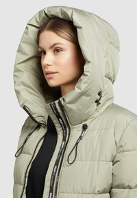 Chaqueta acolchada en verde claro con una gran capucha, cierre de cremallera, detalles de cordón y una etiqueta de marca a lo largo de la cremallera. Textura suave.