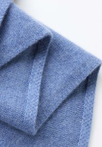 Écharpe tricotée bleu clair en laine douce. Présente une texture confortable avec des coutures visibles et des plis superposés.