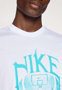Hvid bomulds t-shirt med et turkist, stiliseret "NIKE" logo og baskethåndsgraphic, rund halsudskæring og glat tekstur.