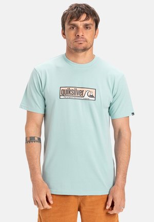 Camiseta de manga corta en color verde menta con el logo de Quiksilver en un diseño rectangular; tela suave y cuello redondo, combinada con pantalones cortos de pana beiges.
