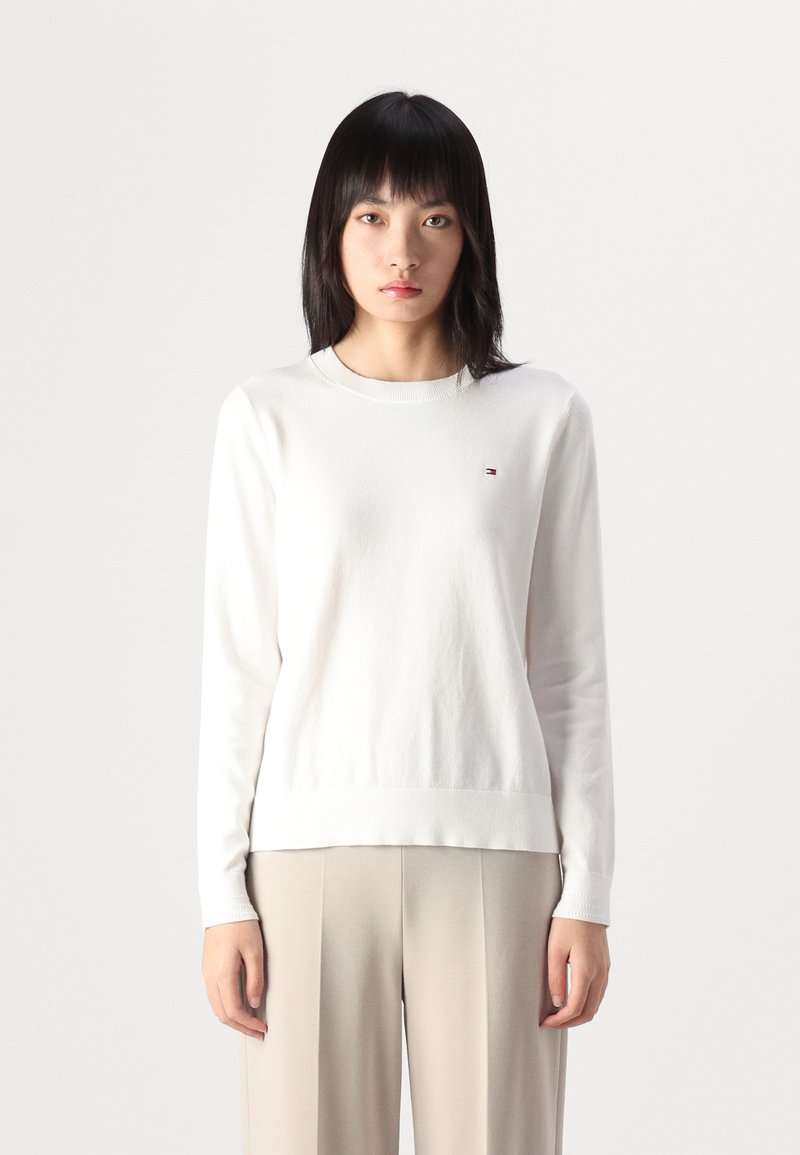 Maglione bianco a maniche lunghe con scollatura rotonda, tessuto testurizzato e un piccolo logo sul lato sinistro del petto. Abbinarlo a pantaloni beige chiaro.