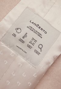 Etykieta produktu Lancerto, z jasnobeżowym materiałem, szczegółami z mieszanki wełny, ikonami przedstawiającymi komfort termiczny, elastycznym materiałem oraz instrukcją pielęgnacji.