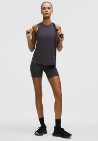 Cămașă sportivă gri fără mâneci și pantaloni scurți asortați, realizate dintr-un material ușor. Modelul ține o coardă de sărit, purtând încălțăminte sportivi și șosete negre.