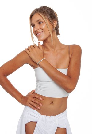 Hvid, kort tanktop og hvid, omslagsnederdel. Glat stof. Ingen mønstre. Blå perlearmbånd på håndleddet. Lys baggrund. Naturlig hudtone.