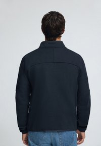 Mörk marinblå fleecejacka med hög krage, texturerad tyg och sänkt axelsöm, kombinerad med ljusblå denimjeans.