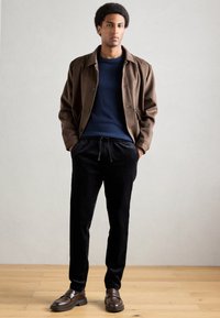 Casaco castanho de botão por cima de um suéter azul-marinho, combinado com calças de veludo cotelê pretas e mocassins castanhos. Texturas suaves, corte casual e tons neutros.