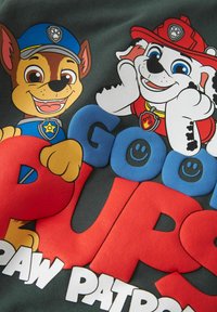 Temno siva tkanina z barvnimi, izbočenimi upodobitvami dveh risanih psov, enega v modri uniformi in drugega z rdečo gasilsko čelado, z izrazitim besedilom.