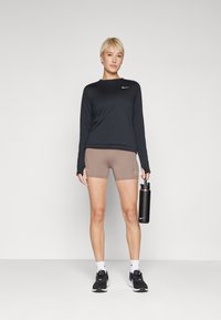 Camiseta deportiva de manga larga negra, pantalones cortos beige, zapatillas negras y una botella de agua negra con pajita. Diseño sencillo con el logo de Nike en la camiseta.