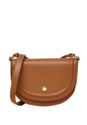 Kvinde iført en striped knaptrøje, hvide bukser, hvide loafers og en brun skuldertaske, stående sidelæns mod en beige baggrund.