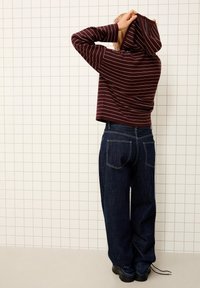 Hoodie à rayures bordeaux avec une capuche ajustée, associé à un jean en denim foncé ample. Présente des coutures contrastées et une silhouette décontractée.