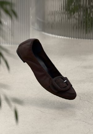 Brown leather ballet flat with a rounded toe, featuring a large buckle detail and a flat sole, set against a neutral background.