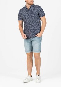 Short-sleeve, dark blue shirt with a white floral pattern, paired with light blue rolled hem shorts and white sneakers.